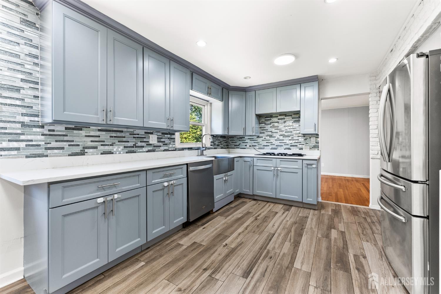 Kitchen with blue-gray cabinets, mosaic tile backsplash, stainless steel appliances, and wood-look flooring.