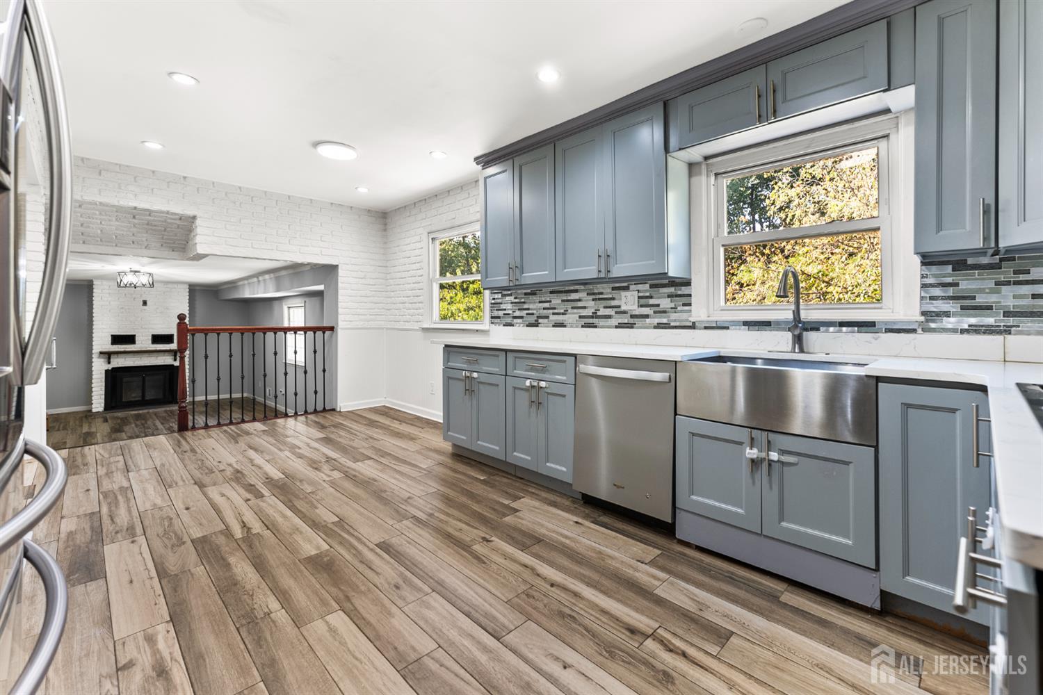 Kitchen with blue-gray cabinets, stainless steel appliances, and a white brick fireplace beyond.