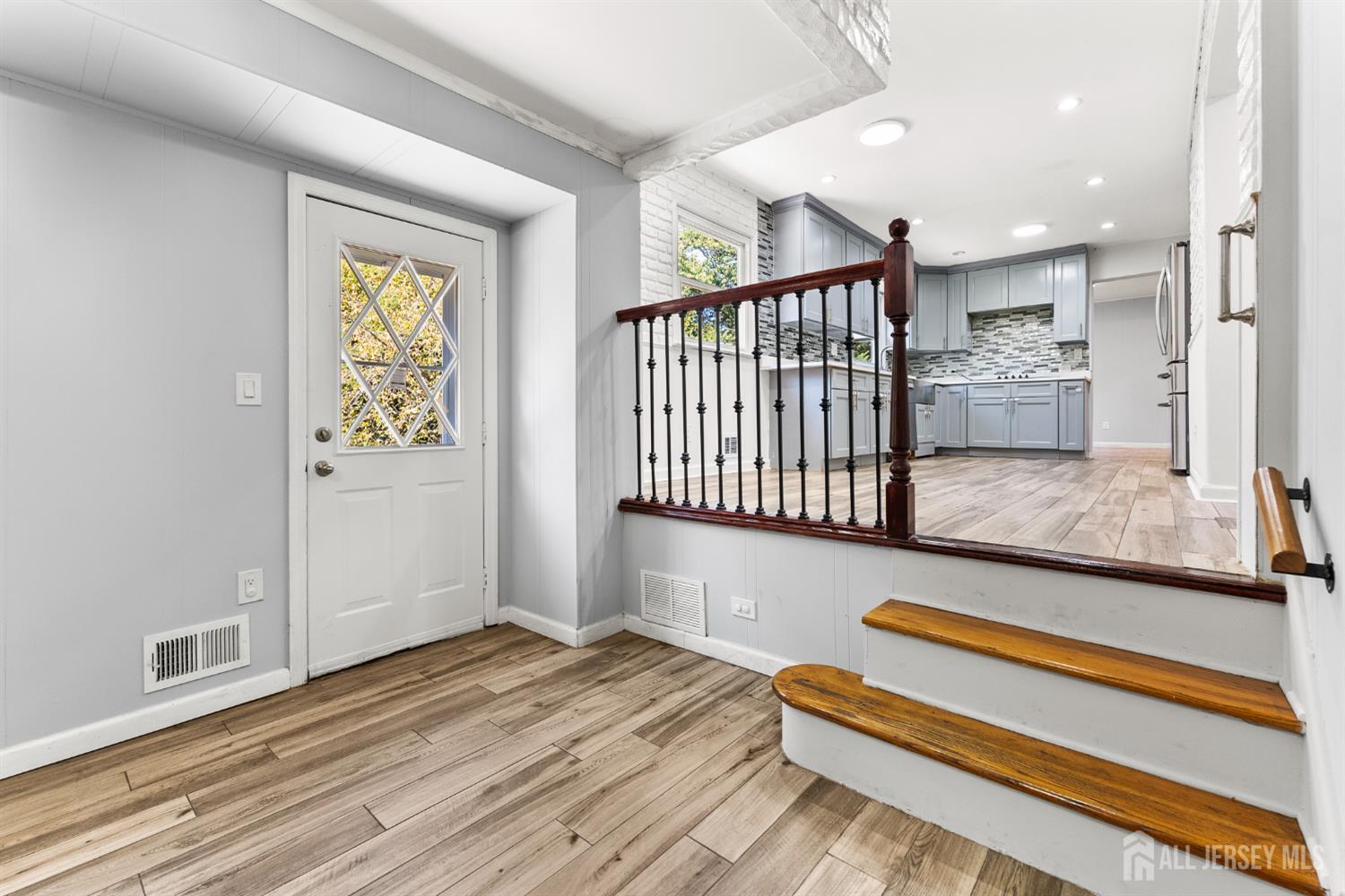 Entry foyer with wood-look tile flooring, raised kitchen, and dark wood and metal railing.