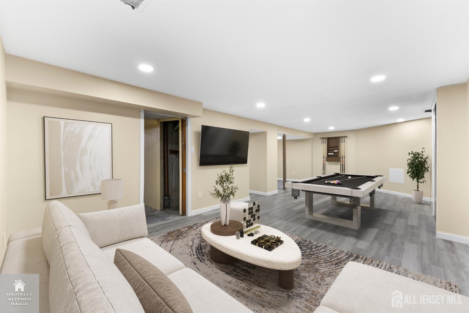 Staged basement recreation room with a pool table, cream sectional sofa, and wall-mounted television.
