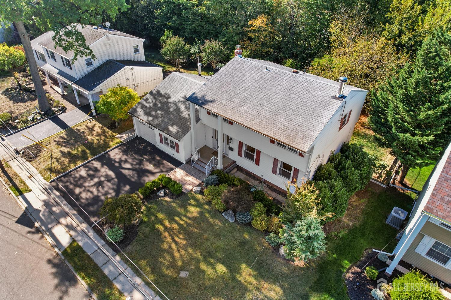 Aerial view of a white-sided home with a broad roof, driveway, and landscaped yard.