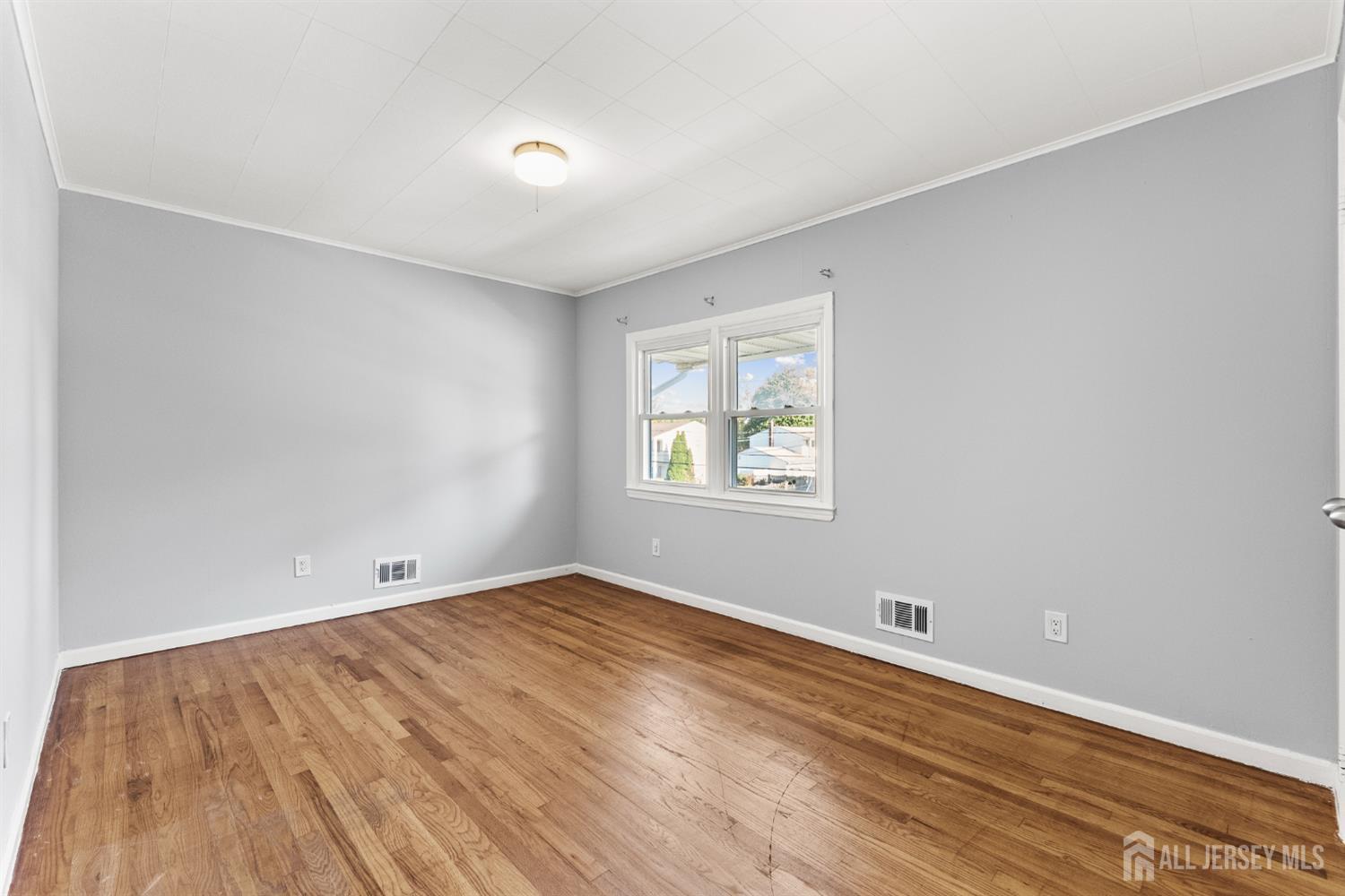Vacant bedroom with hardwood floors, gray walls, and a double window.