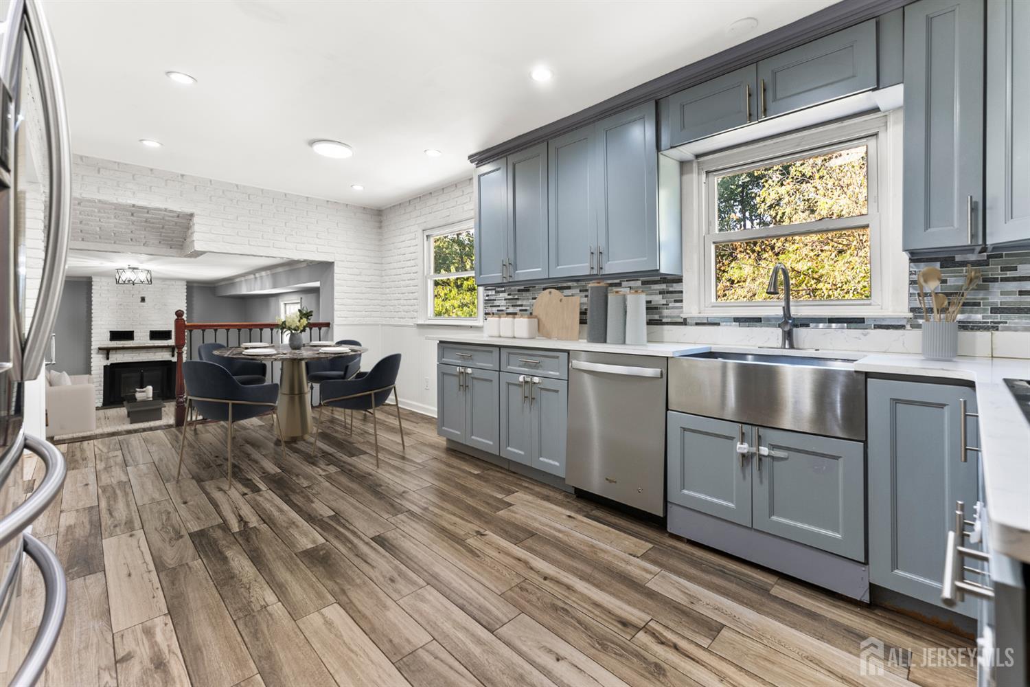 Blue-gray kitchen with stainless appliances and a large sink, opening to a dining area and fireplace.