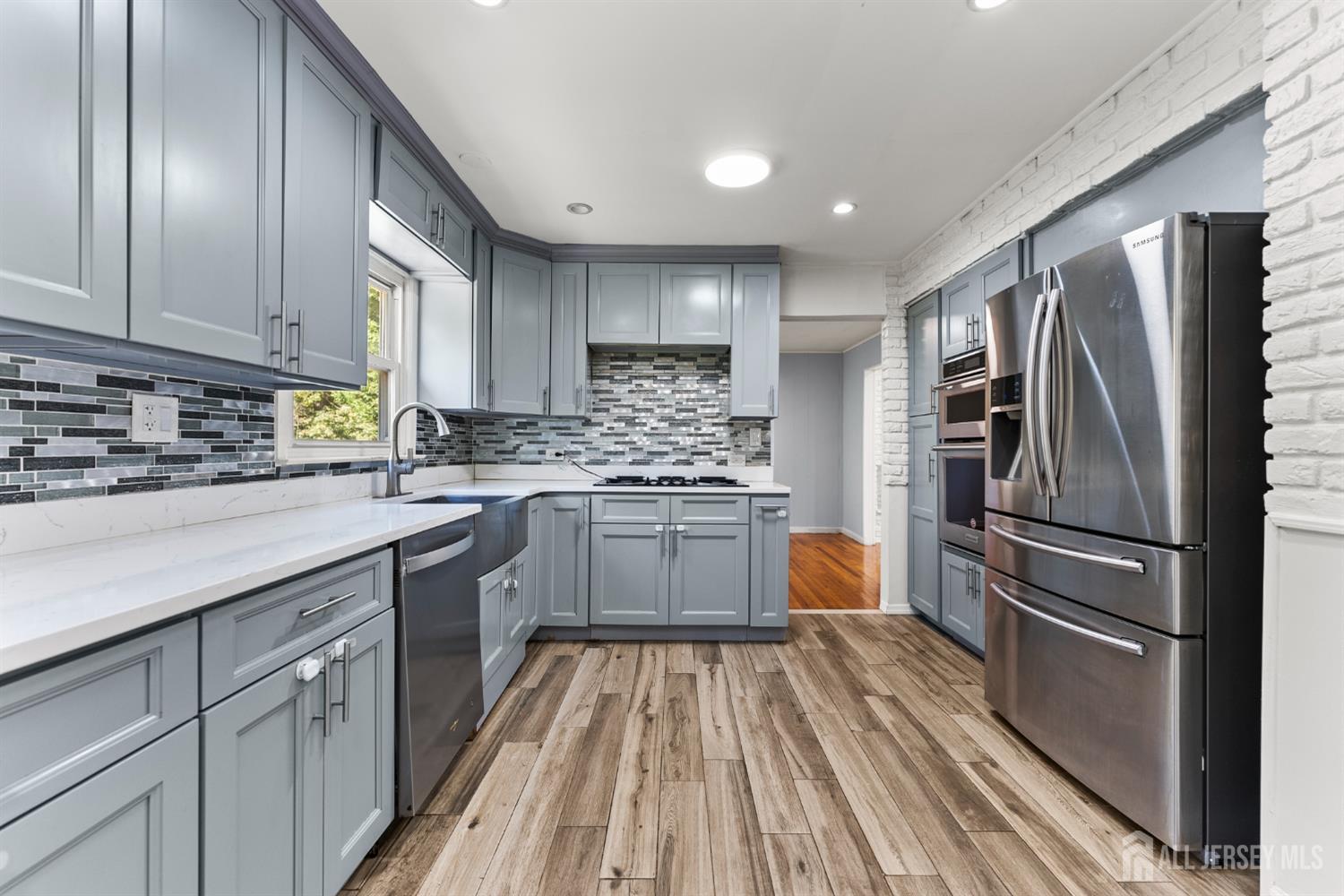 Kitchen with gray cabinets, stainless steel appliances, a mosaic tile backsplash, and wood-look flooring.