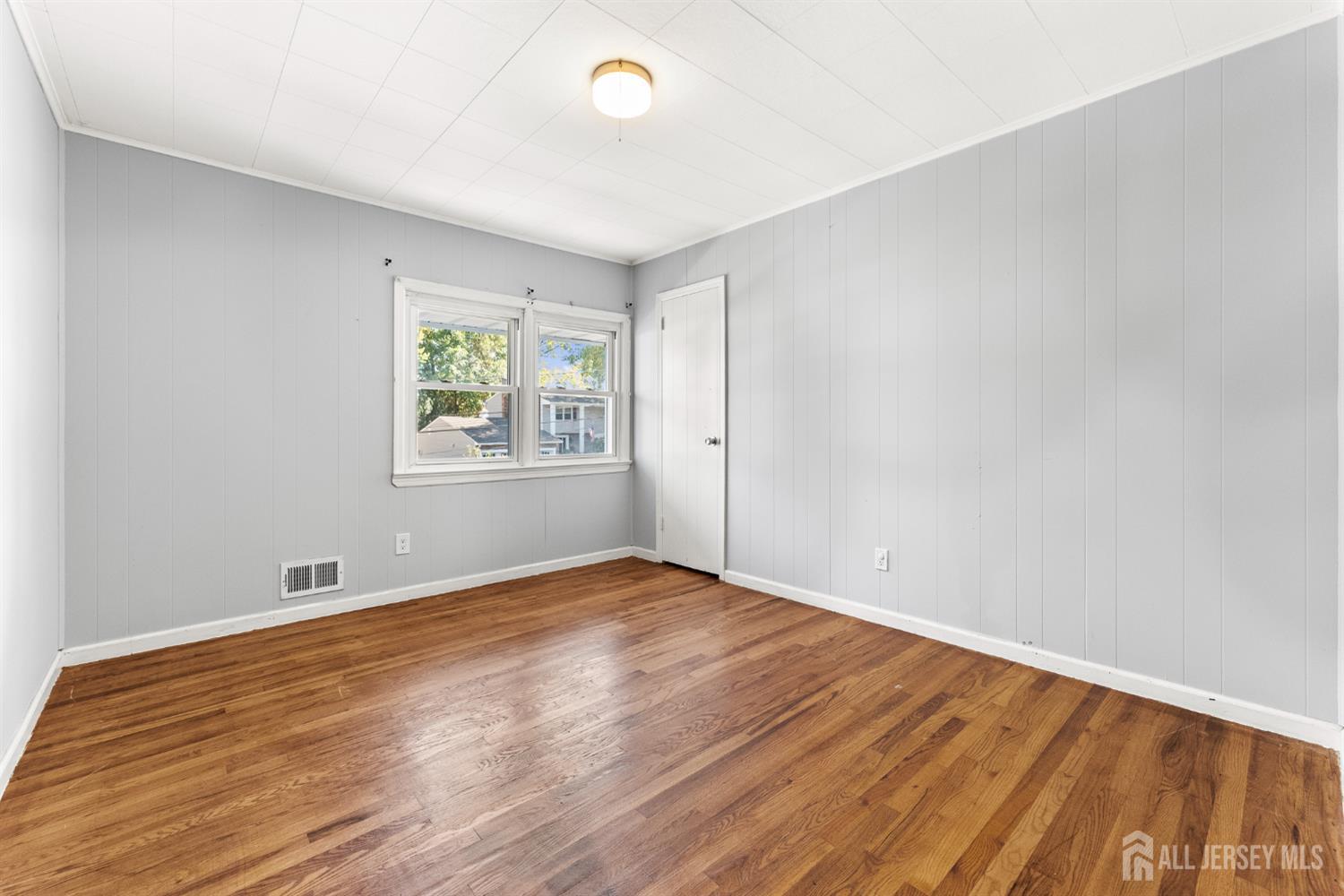 Empty room with gray paneled walls, hardwood floors, and a double window.