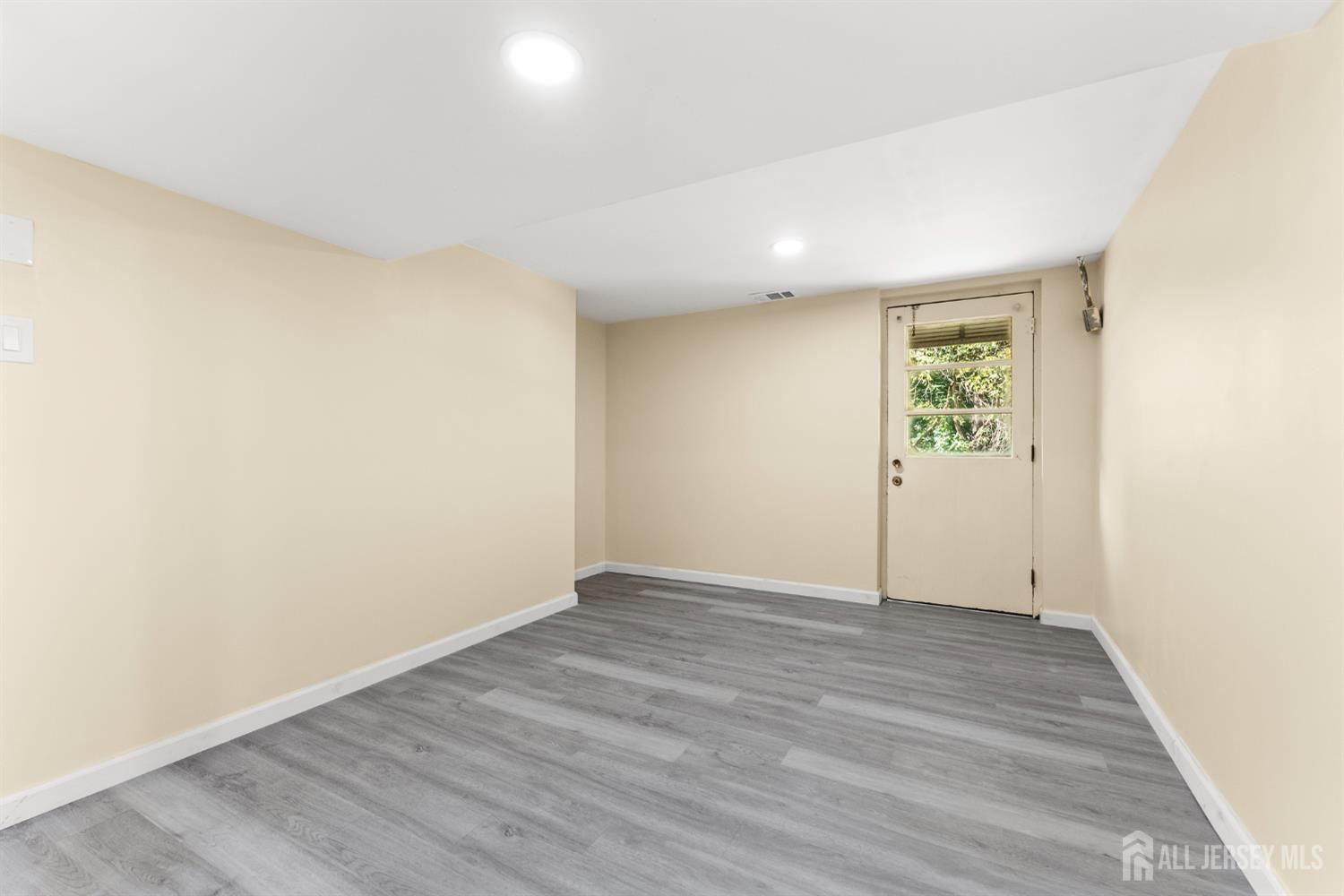 Empty room with gray plank flooring and a glazed door looking out onto greenery.
