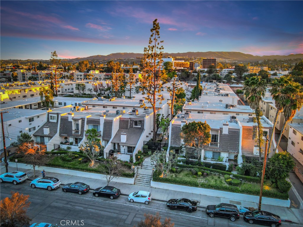 Aerial view of attached homes along a street, with hills in the distance at sunset.