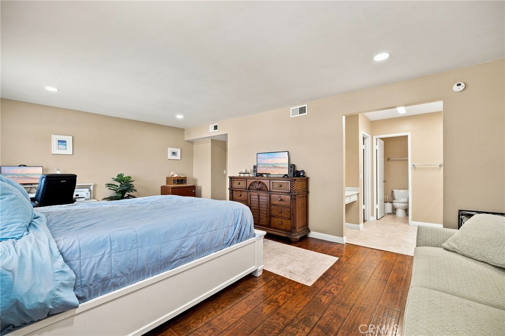 Bedroom with a blue bedspread, wooden dresser, desk, and adjoining bathroom.