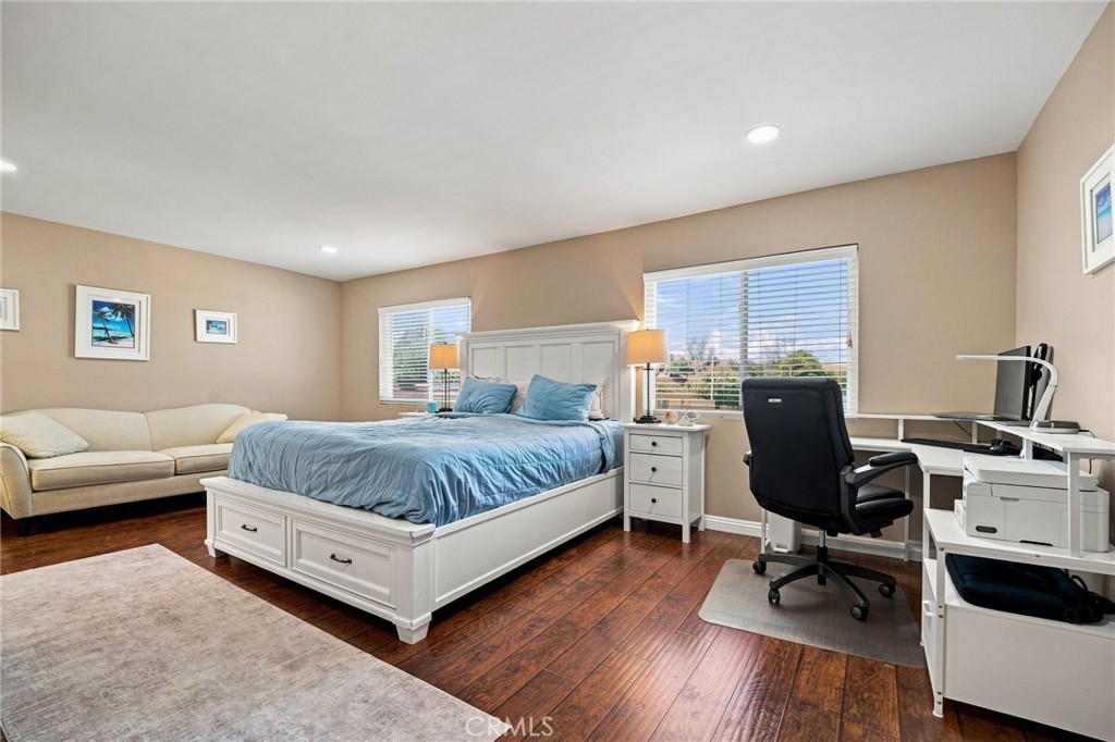 Bedroom with blue bedding, a cream sofa, and a white computer desk beside two windows.
