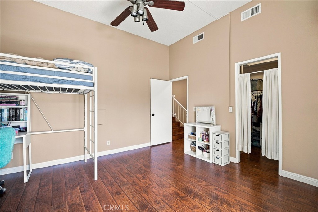 Bedroom with a white loft bunk bed, dark wood flooring, and a curtained closet.