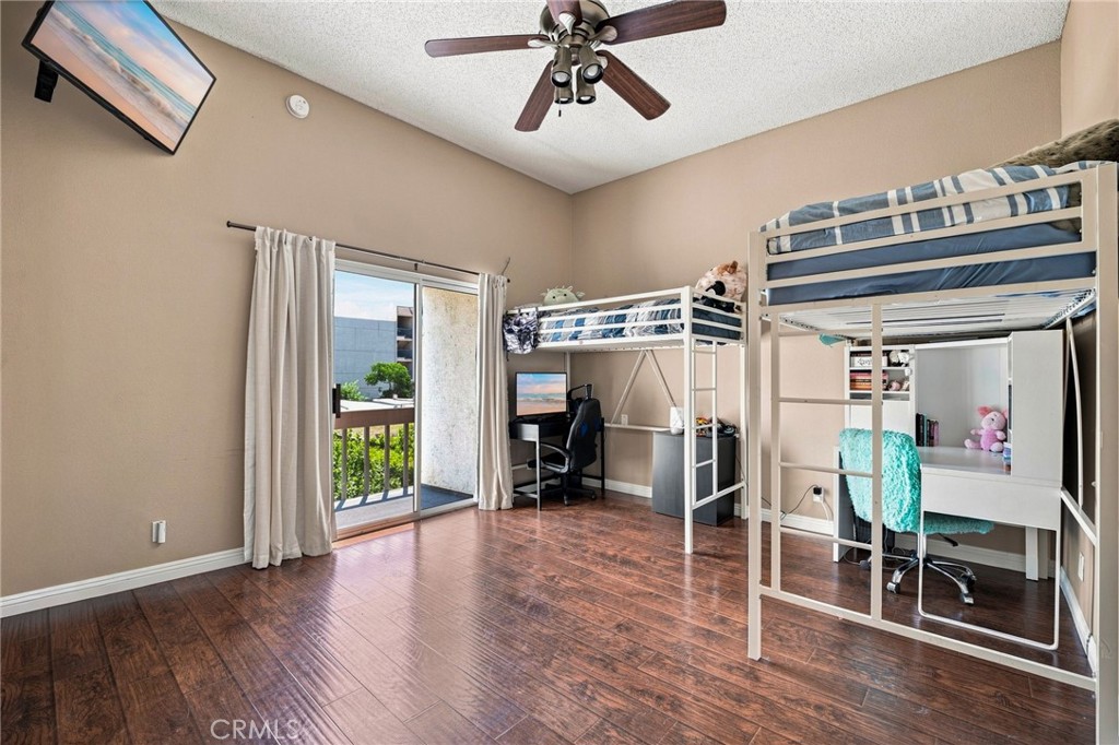 Bedroom with two loft beds and desks, opening onto a balcony through a sliding glass door.