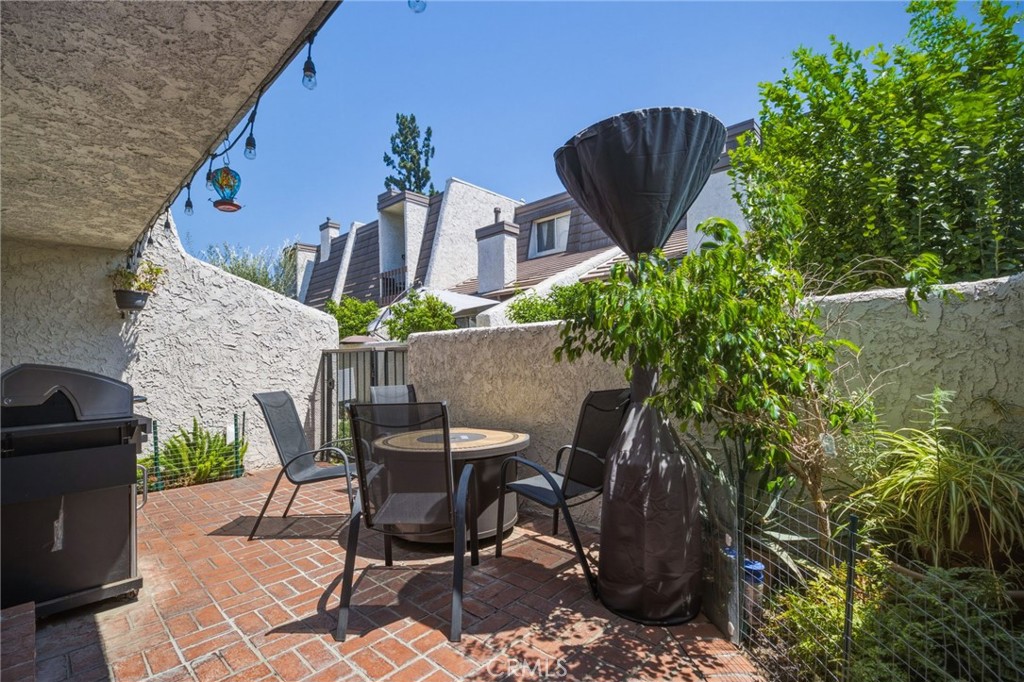 Outdoor patio with brick pavers, seating, a barbecue grill, and lush greenery.