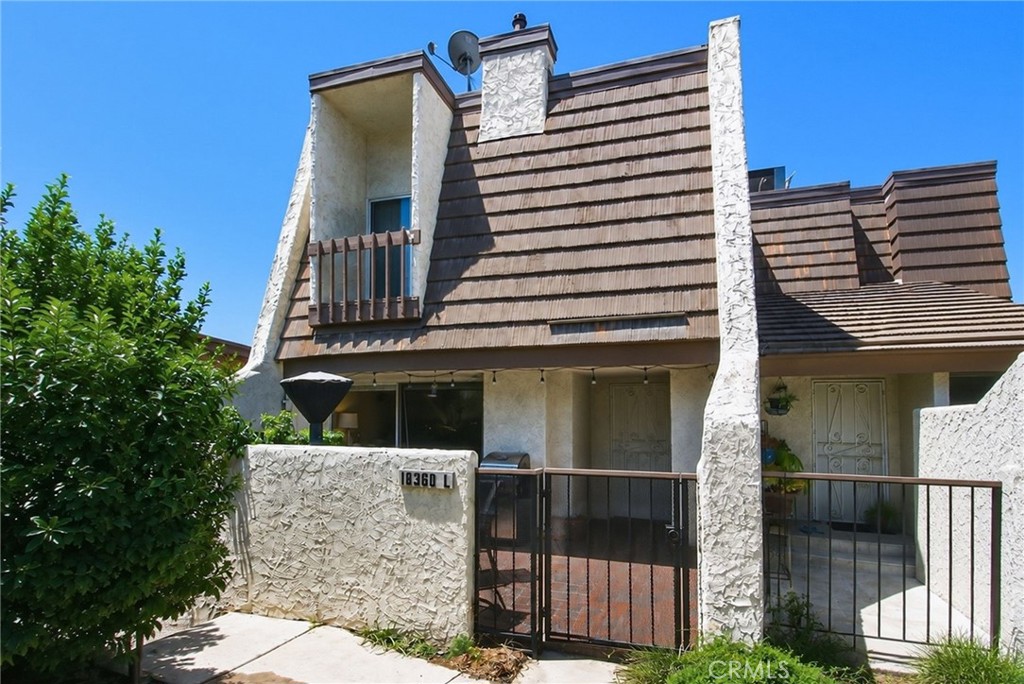 Two-story stucco home with a steep brown roof, small balcony, and gated front entry.