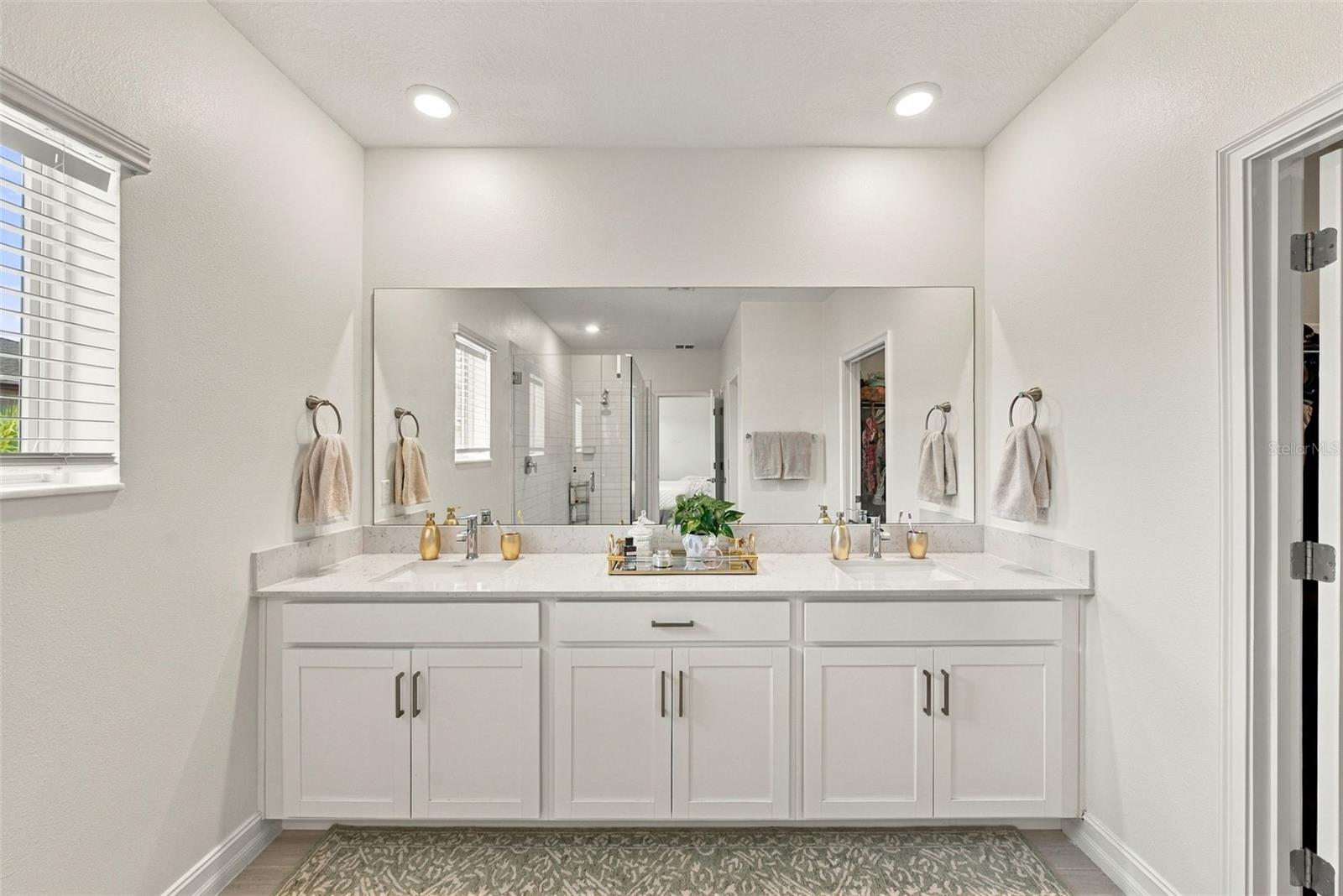 Bathroom with a white double-sink vanity, pale stone counter, and large mirror.