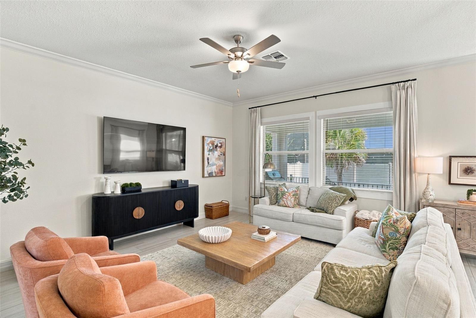 Staged living room with white sofas, coral armchairs, and large curtained windows.