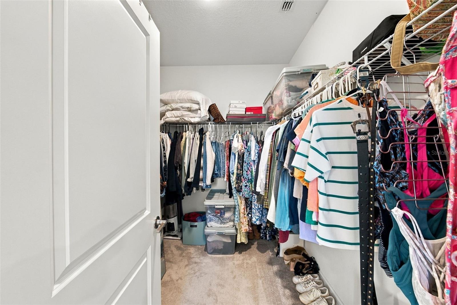 Walk-in closet packed with clothes, with storage bins and folded bedding on shelves.