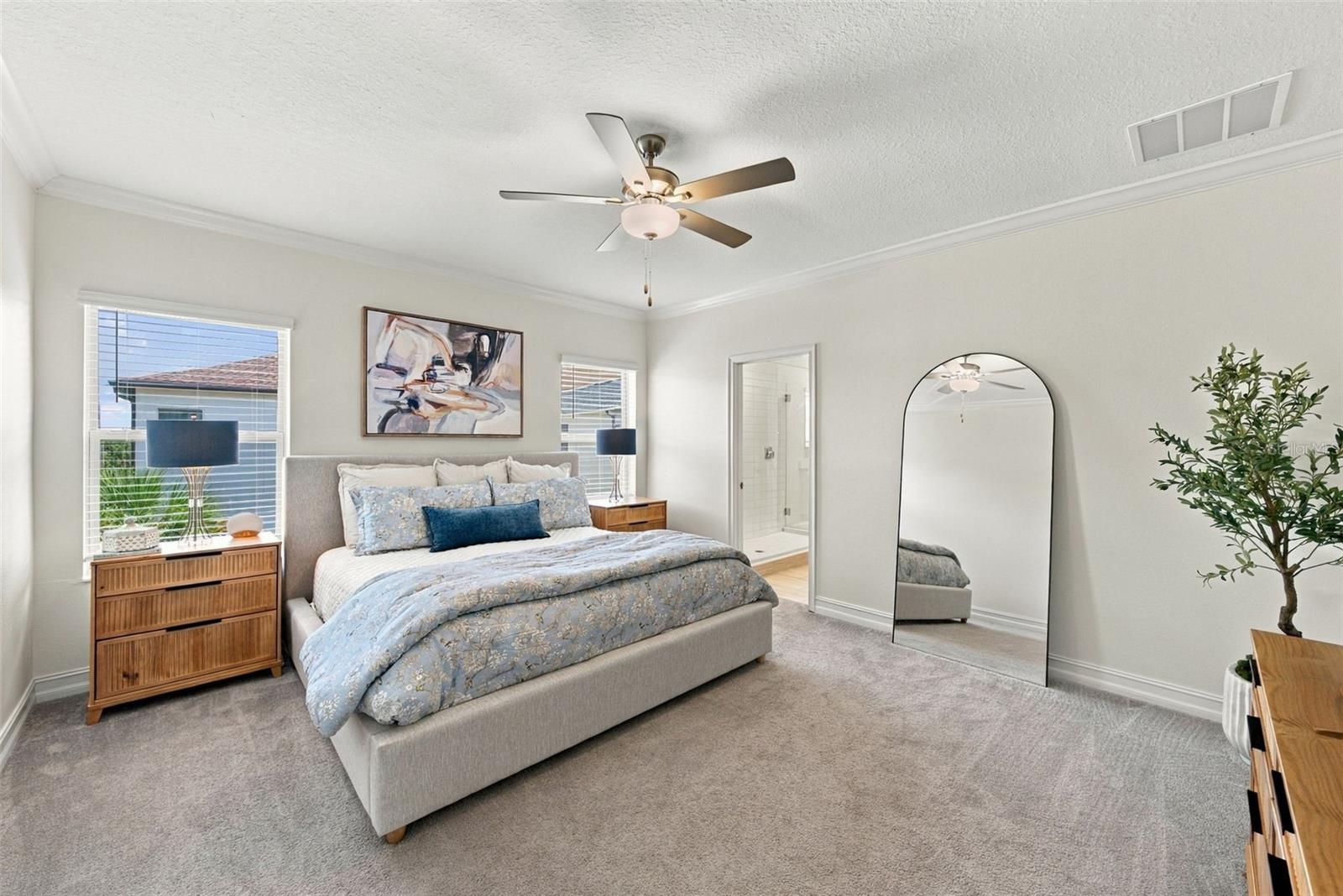Staged bedroom with a king bed, pale blue floral bedding, ceiling fan, and tall arched mirror.