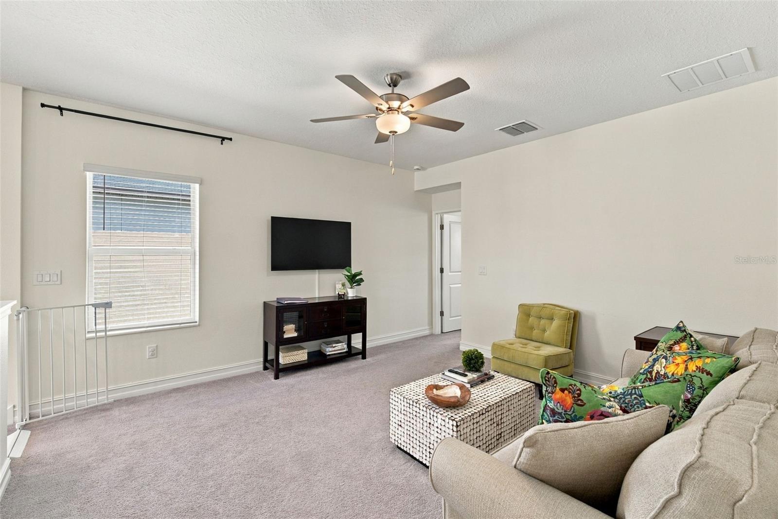 Upstairs living area with a ceiling fan, wall-mounted TV, beige sofa, and green accent chair.