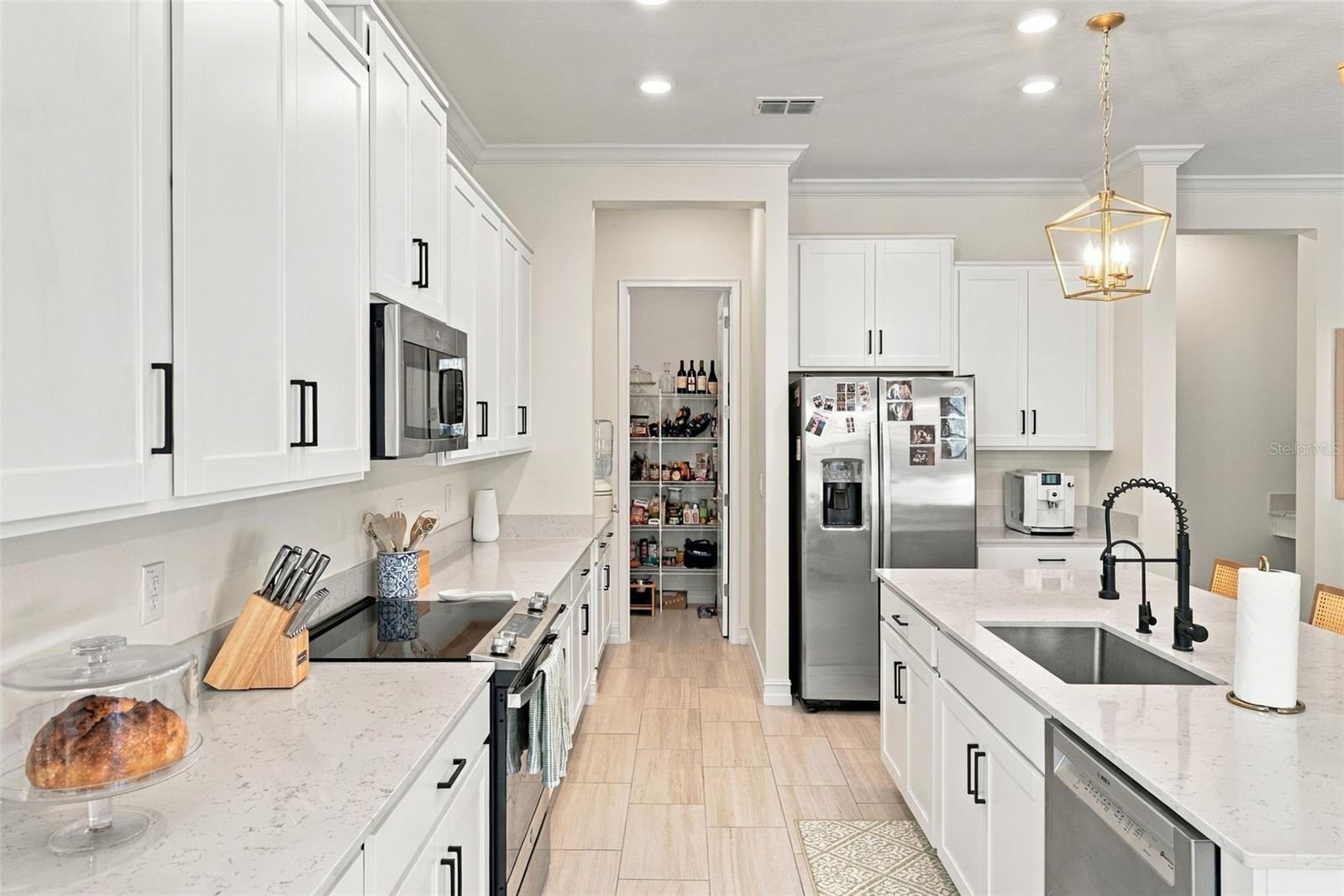 Bright white kitchen with a large island, stainless steel appliances, and a walk-in pantry.