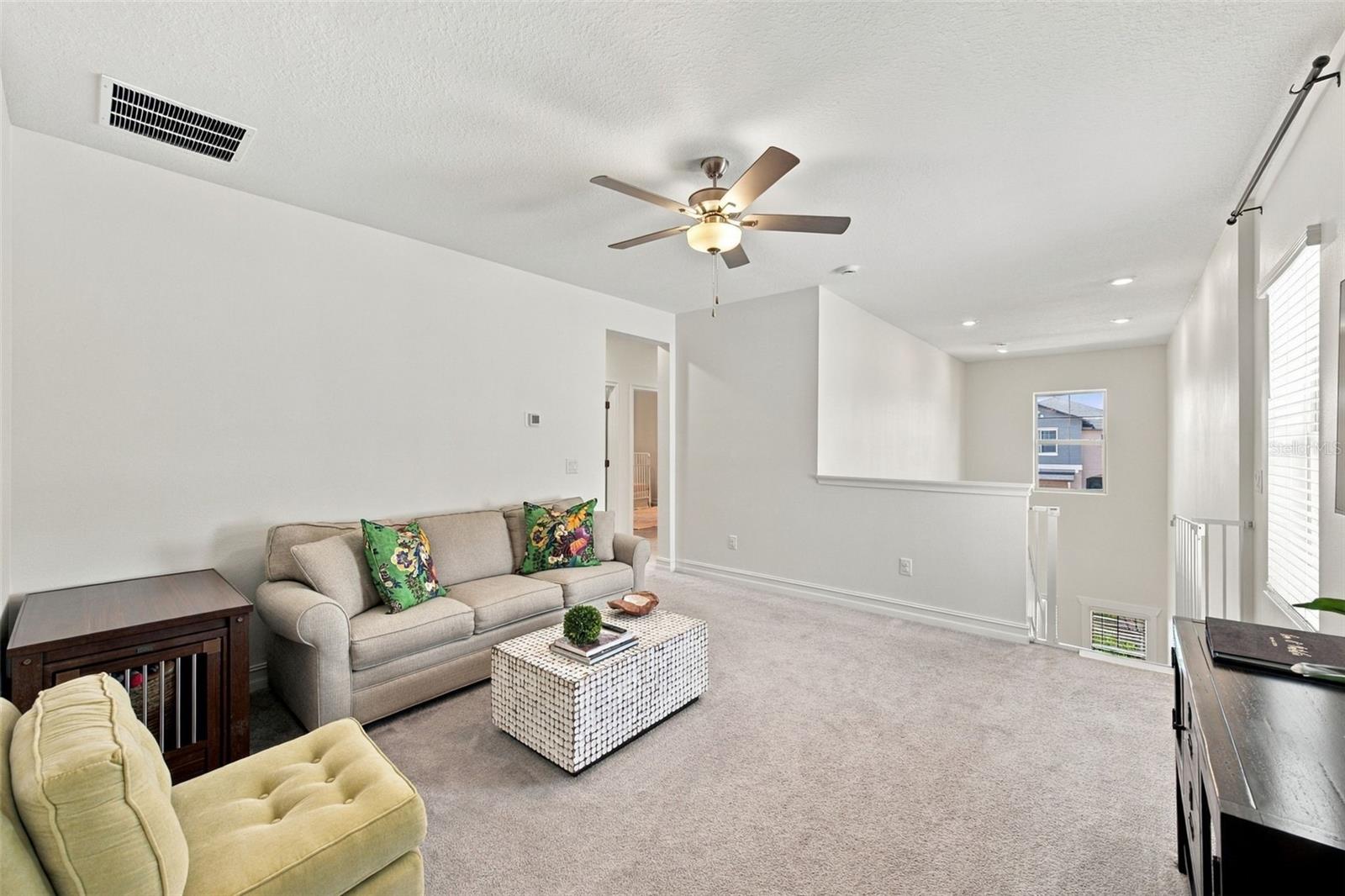 Furnished living room with a beige sofa, patterned coffee table, ceiling fan, and carpeted floor.