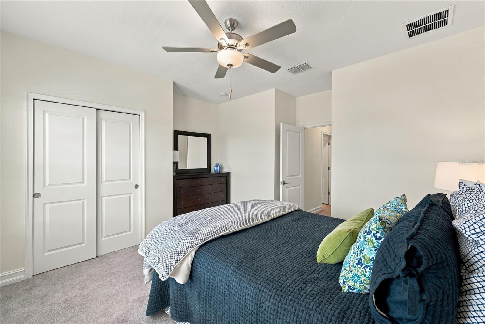 Bedroom with a dark teal quilted bed, patterned pillows, ceiling fan, and mirrored dresser.
