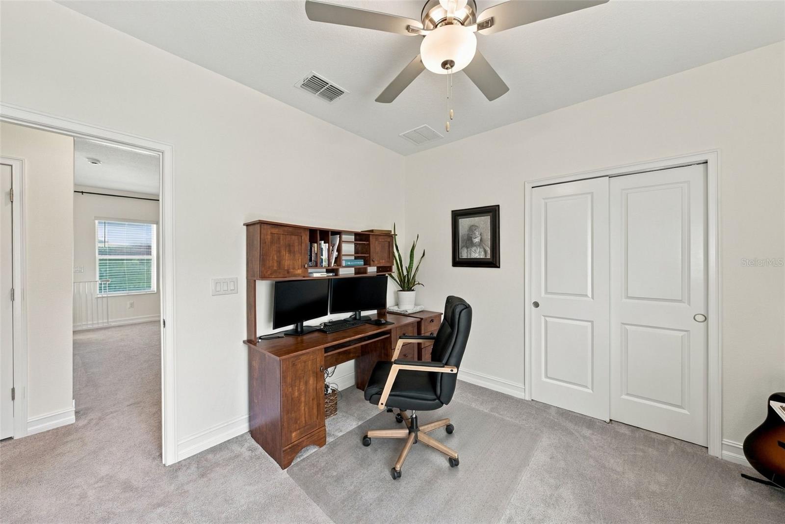 Furnished home office with a wooden desk, dual monitors, and sliding closet doors.