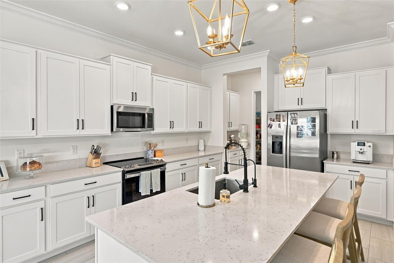 Bright white kitchen with a large stone island, stainless steel appliances, and gold pendant lights.