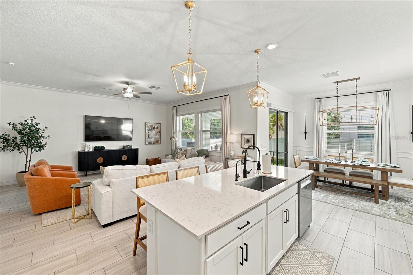 Open-plan kitchen and living area with a large white island, orange armchairs, and dining table by wide windows.