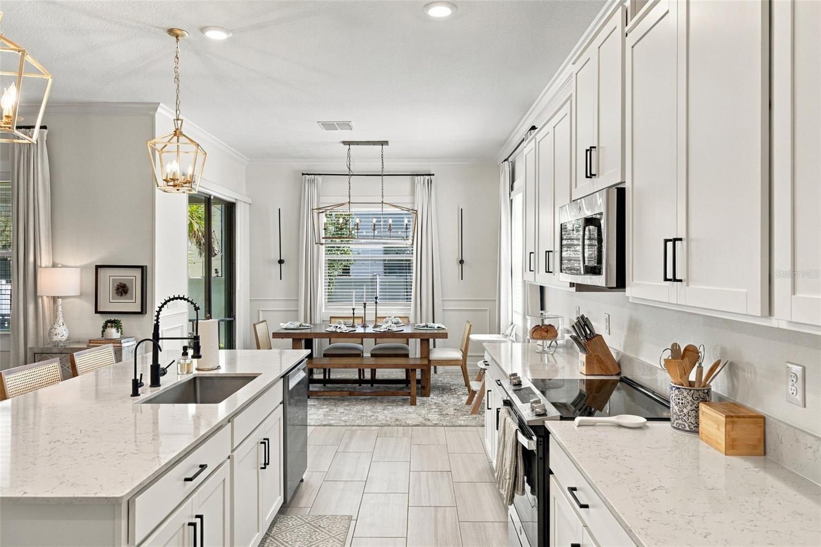 Bright kitchen with a large quartz island, white cabinetry, stainless appliances, and an adjoining dining area.