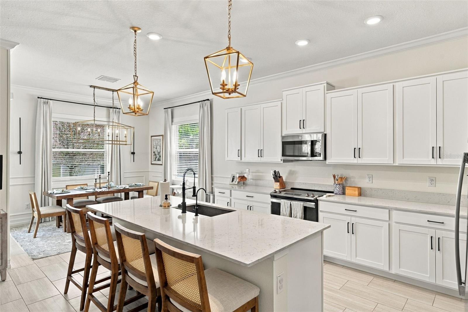 Bright white kitchen with a large quartz island, black sink, stainless appliances, and an adjoining dining area.