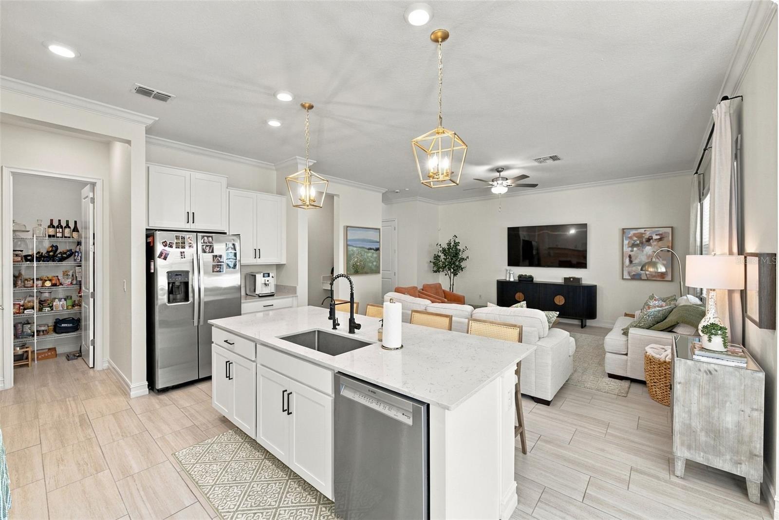 Open-plan kitchen with a large quartz island, white cabinets, stainless steel appliances, and adjoining living room.