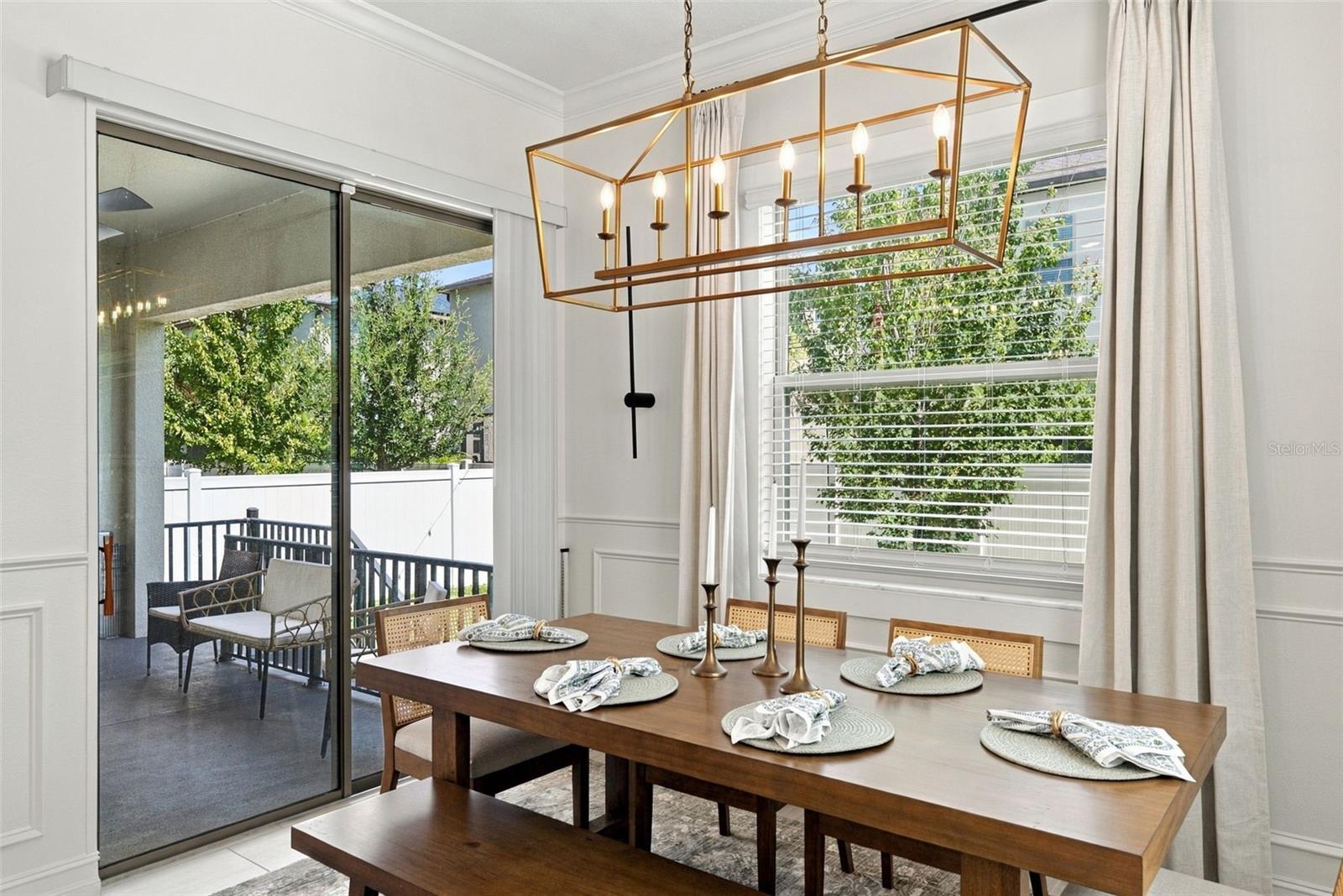 Dining room with a set dark wood table, brass chandelier, and sliding glass doors to a patio.