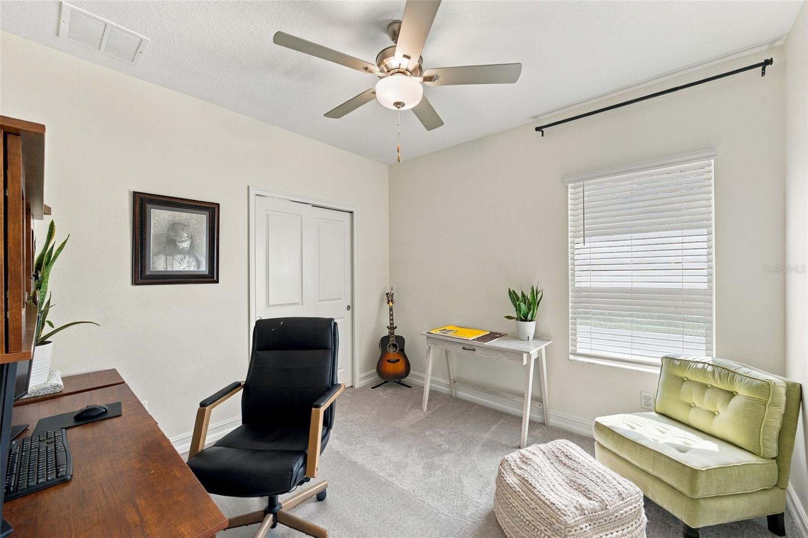 Furnished home office with a wooden desk, green armchair, and ceiling fan.