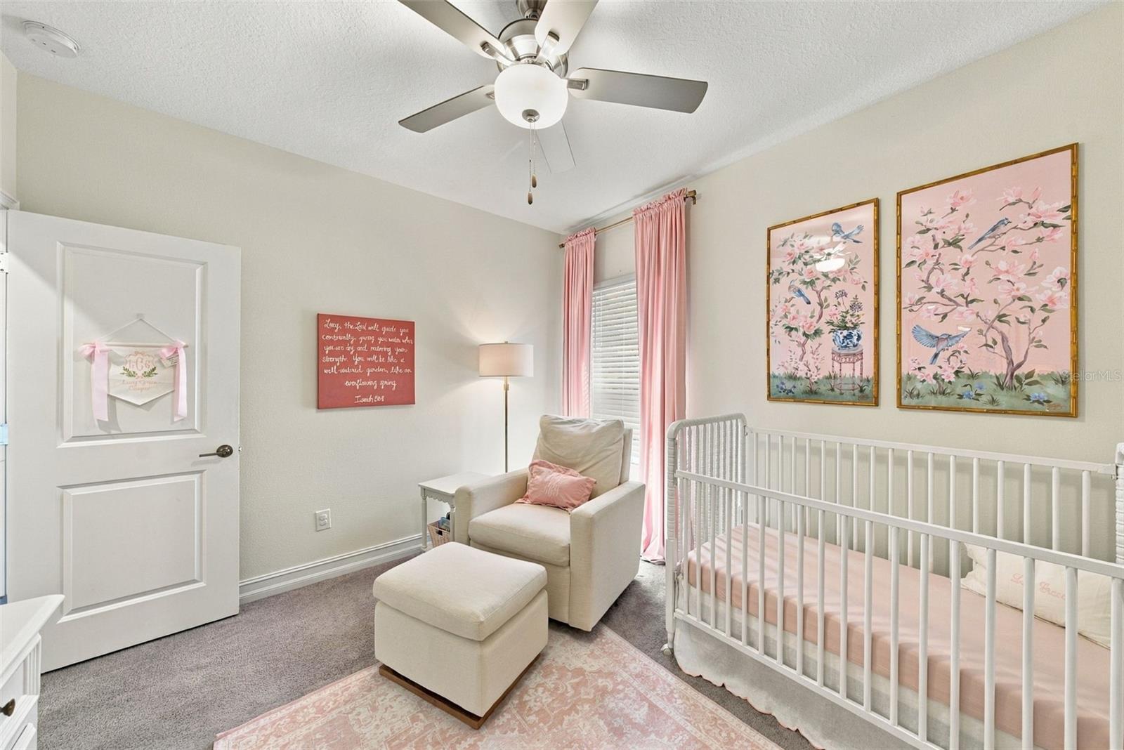 Nursery with white crib, pink bedding and curtains, and a cushioned rocking chair.