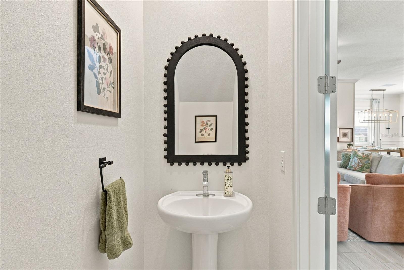 Powder room with a white pedestal sink, black arched mirror, and green hand towel.