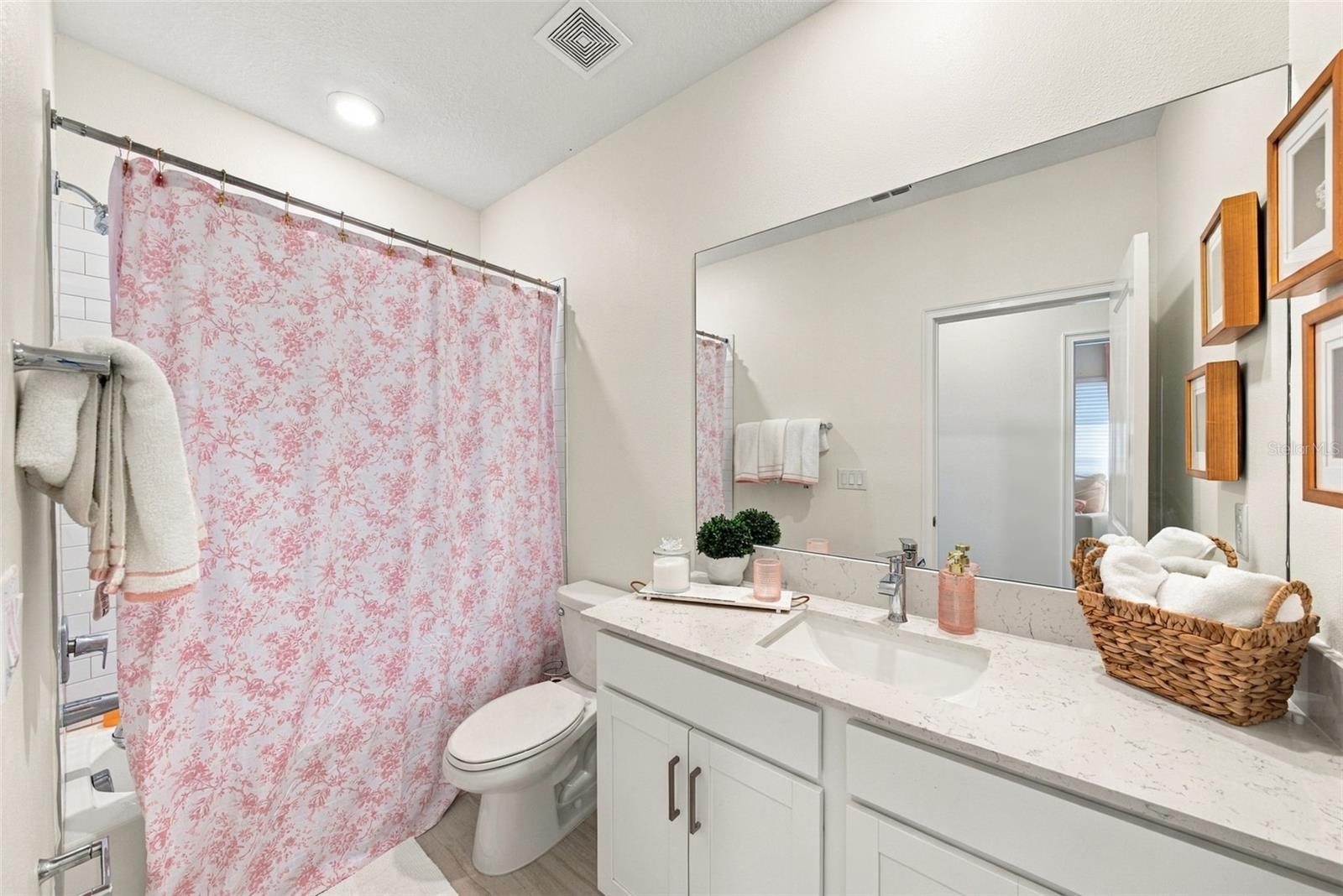 Bathroom with a pink floral shower curtain, white vanity, and large mirror.