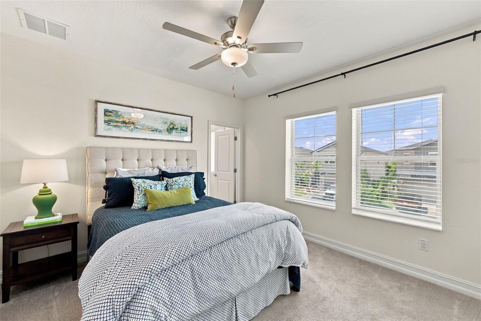 Staged bedroom with navy and white bedding, a tufted headboard, and two bright windows.