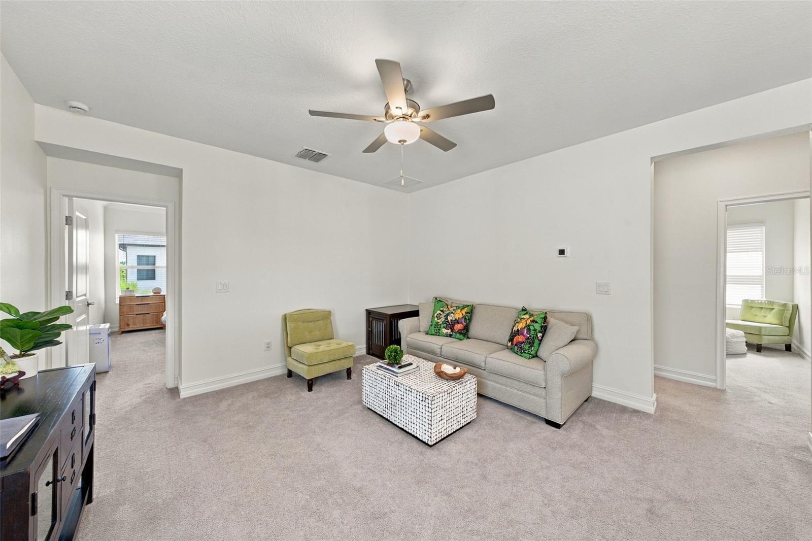 Staged living room with gray sofa, floral pillows, green accent chair, and ceiling fan.