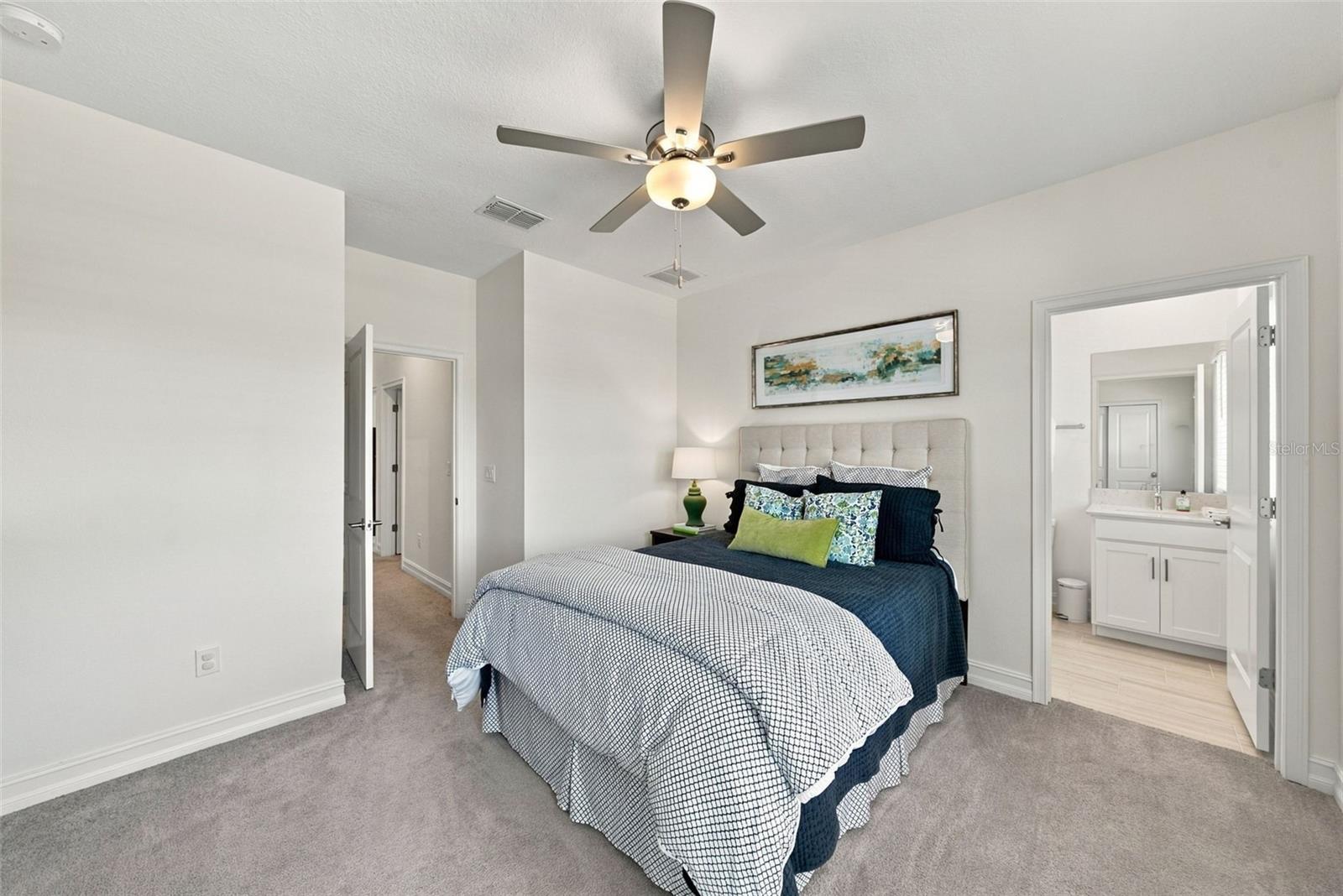 Staged bedroom with navy and white bedding and an open doorway to a bathroom vanity.
