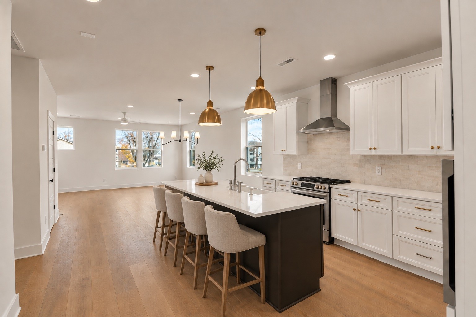 Open-plan kitchen with a dark island, white cabinets, brass pendant lights, and four upholstered bar stools.