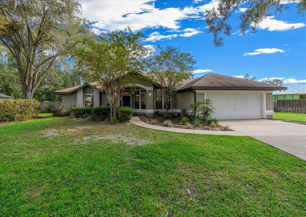 Single-story gray home with an attached garage, covered entry, and broad green lawn.