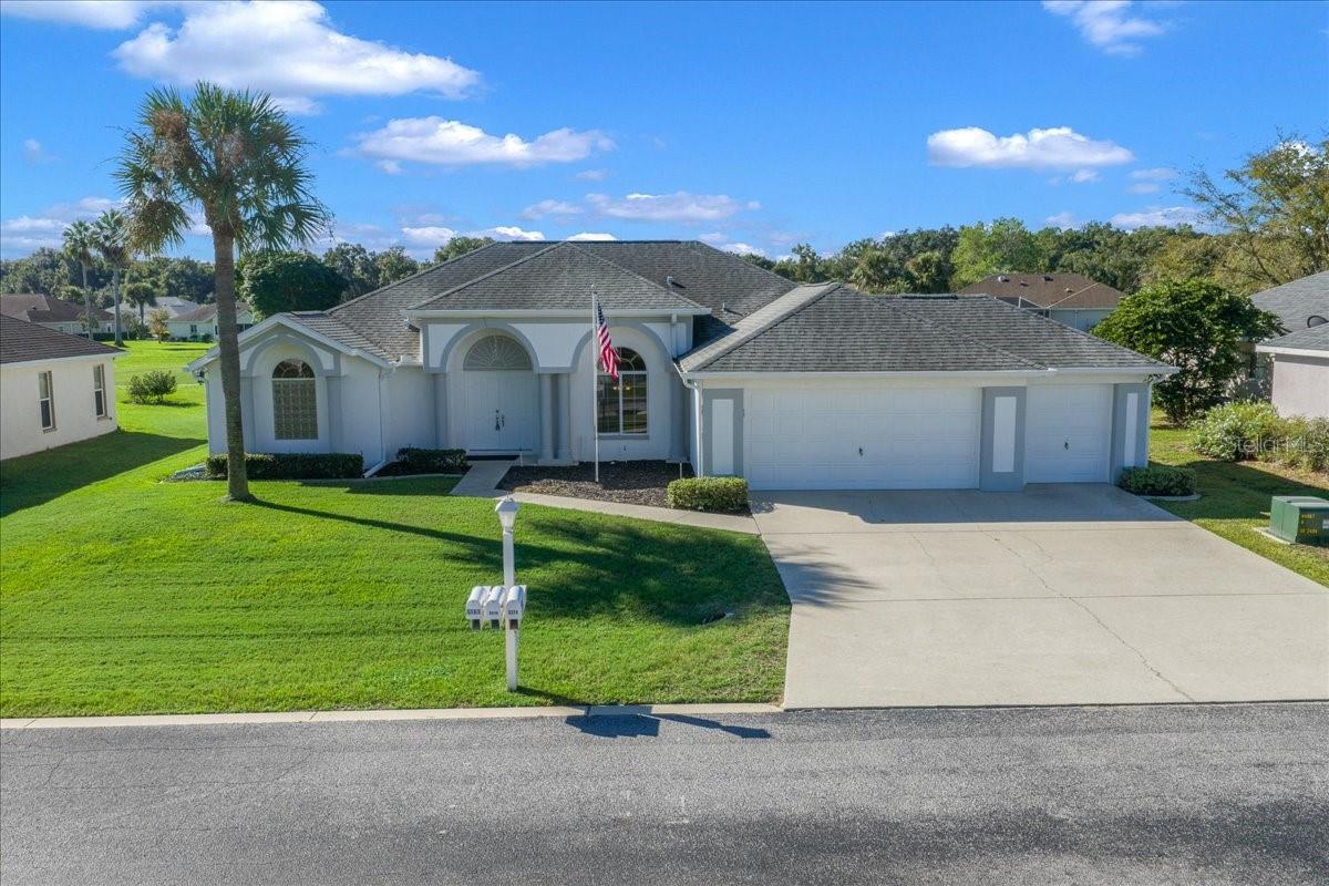 Single-story home with arched windows, a three-car garage, palm tree, and American flag.
