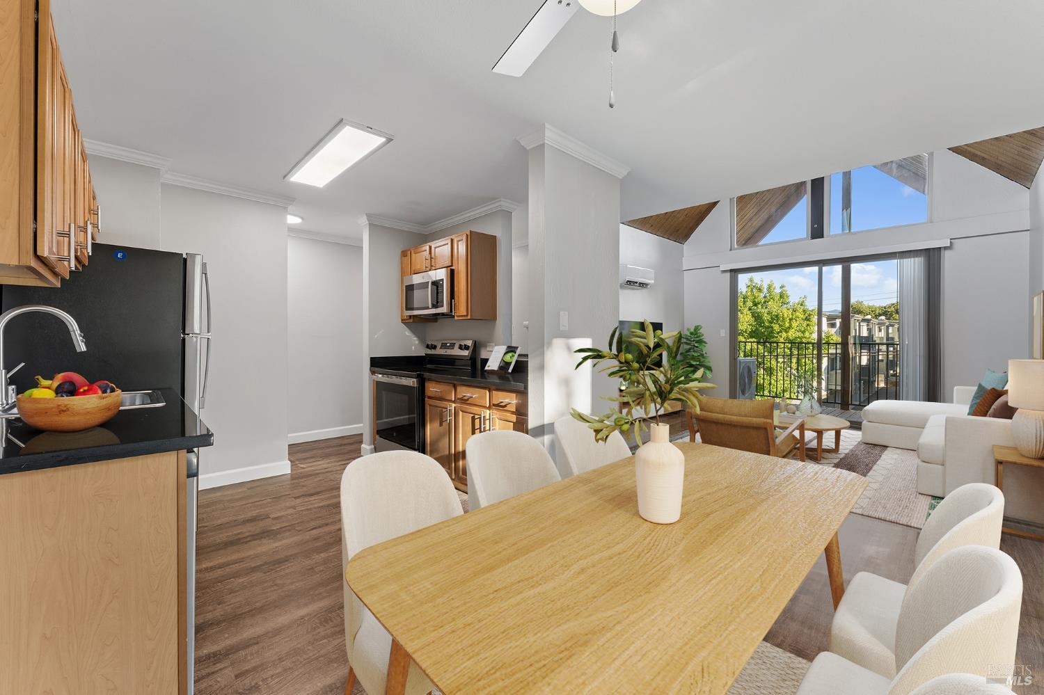Open-plan kitchen and living room with wood cabinetry, vaulted ceiling, and balcony access.