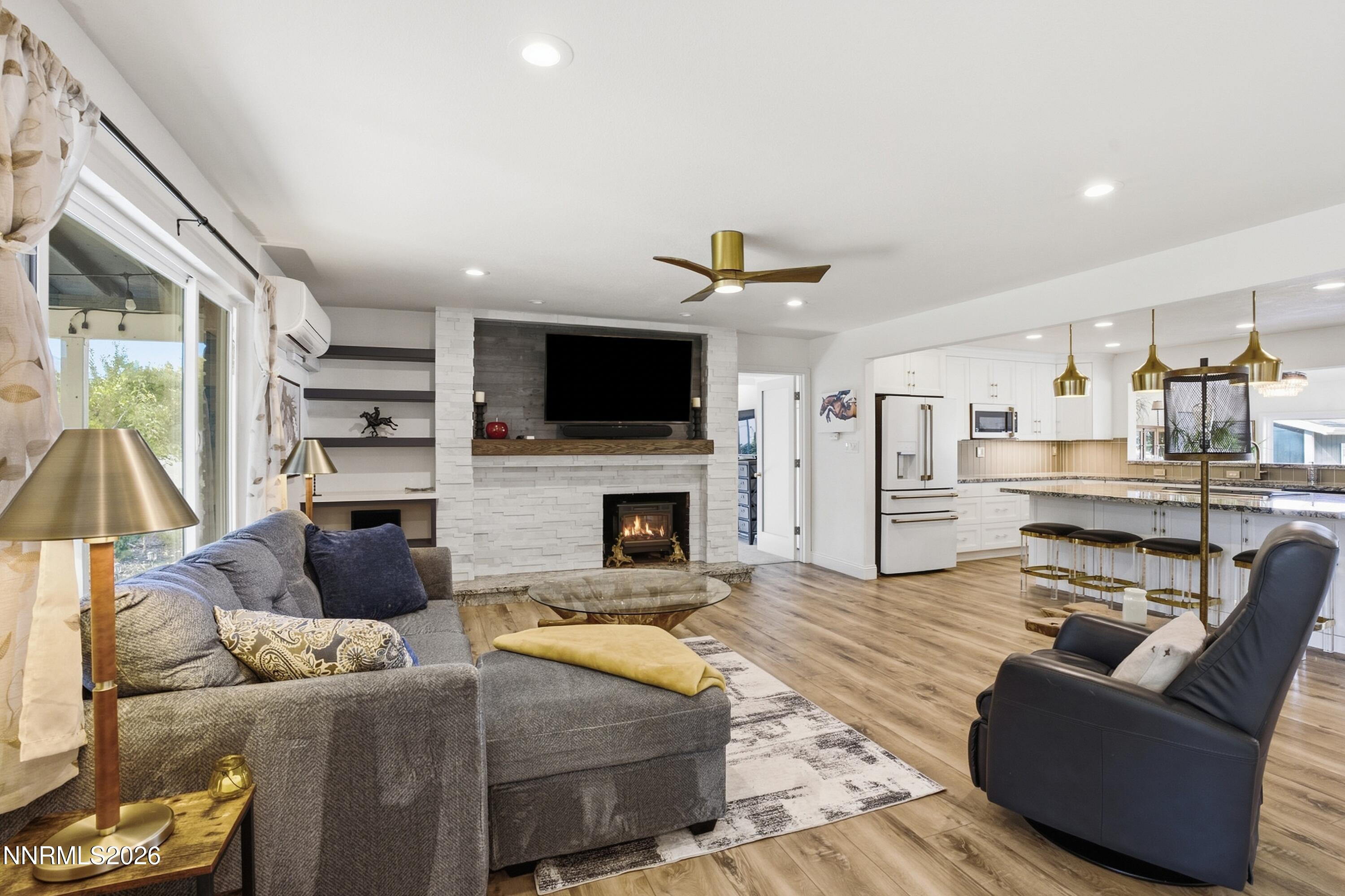 Open-plan living room and kitchen with a stone fireplace, gray sectional, and white cabinetry.