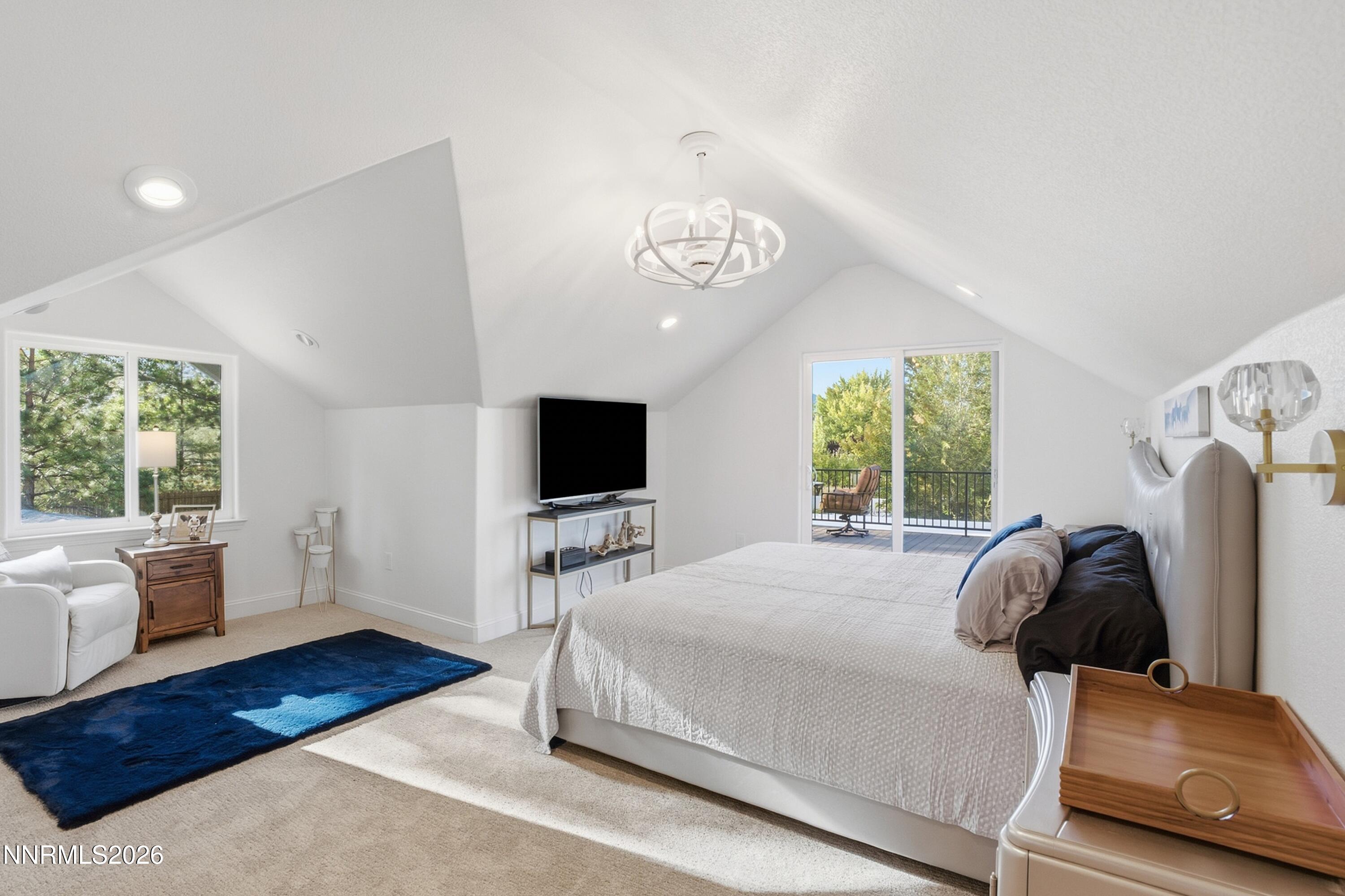 Furnished bedroom with a vaulted ceiling, blue rug, and sliding doors opening to a balcony.