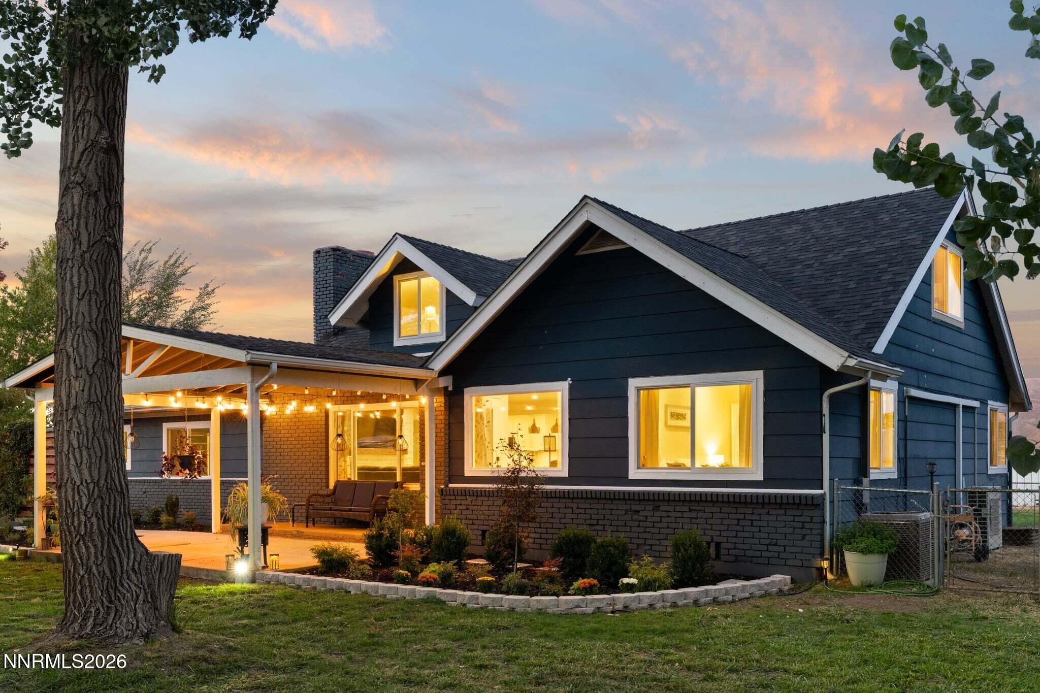 Dark blue gabled house with a covered, string-lit patio at dusk.