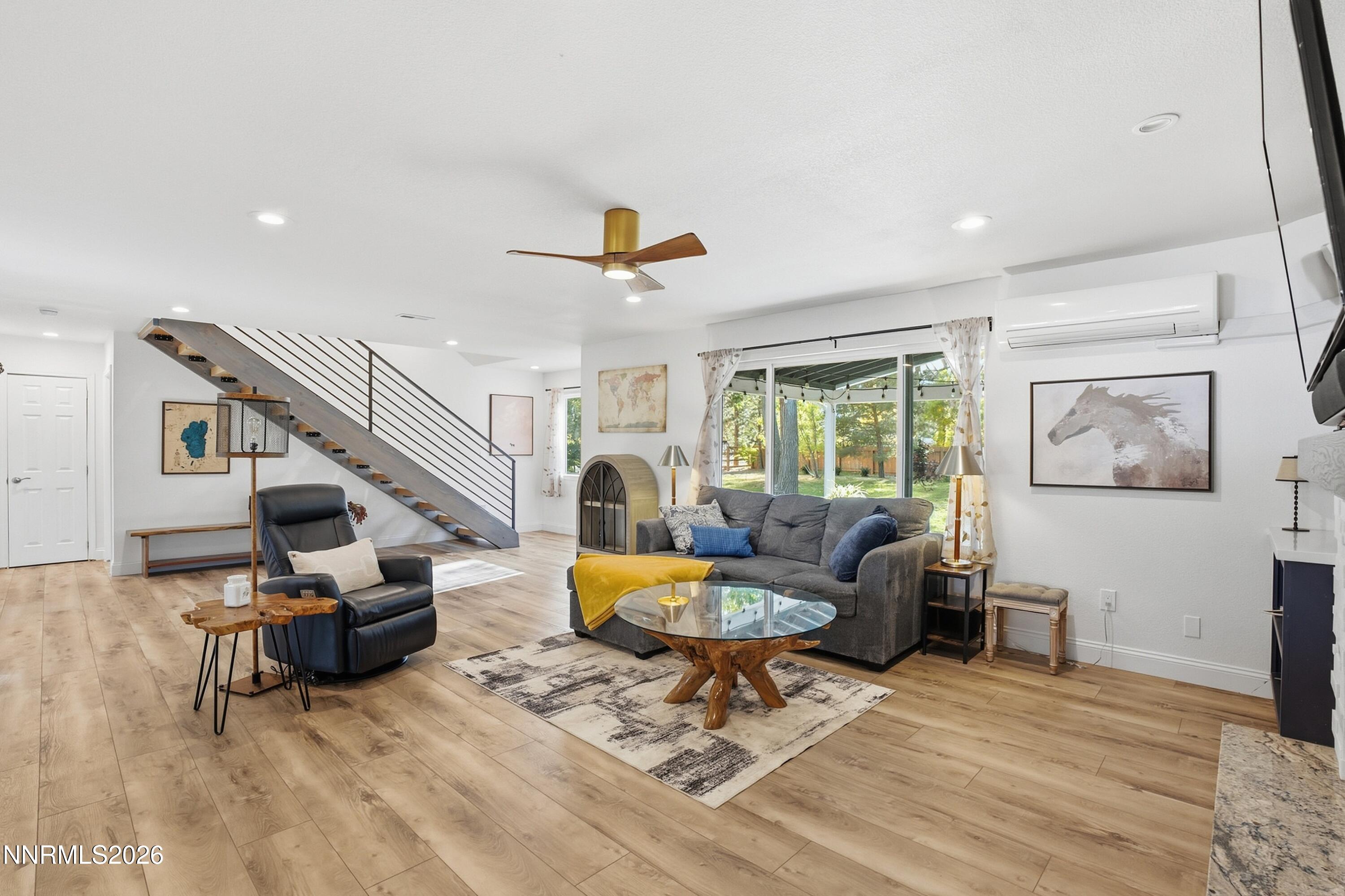 Furnished living room with an open staircase, gray sectional, and sliding doors to a leafy backyard.
