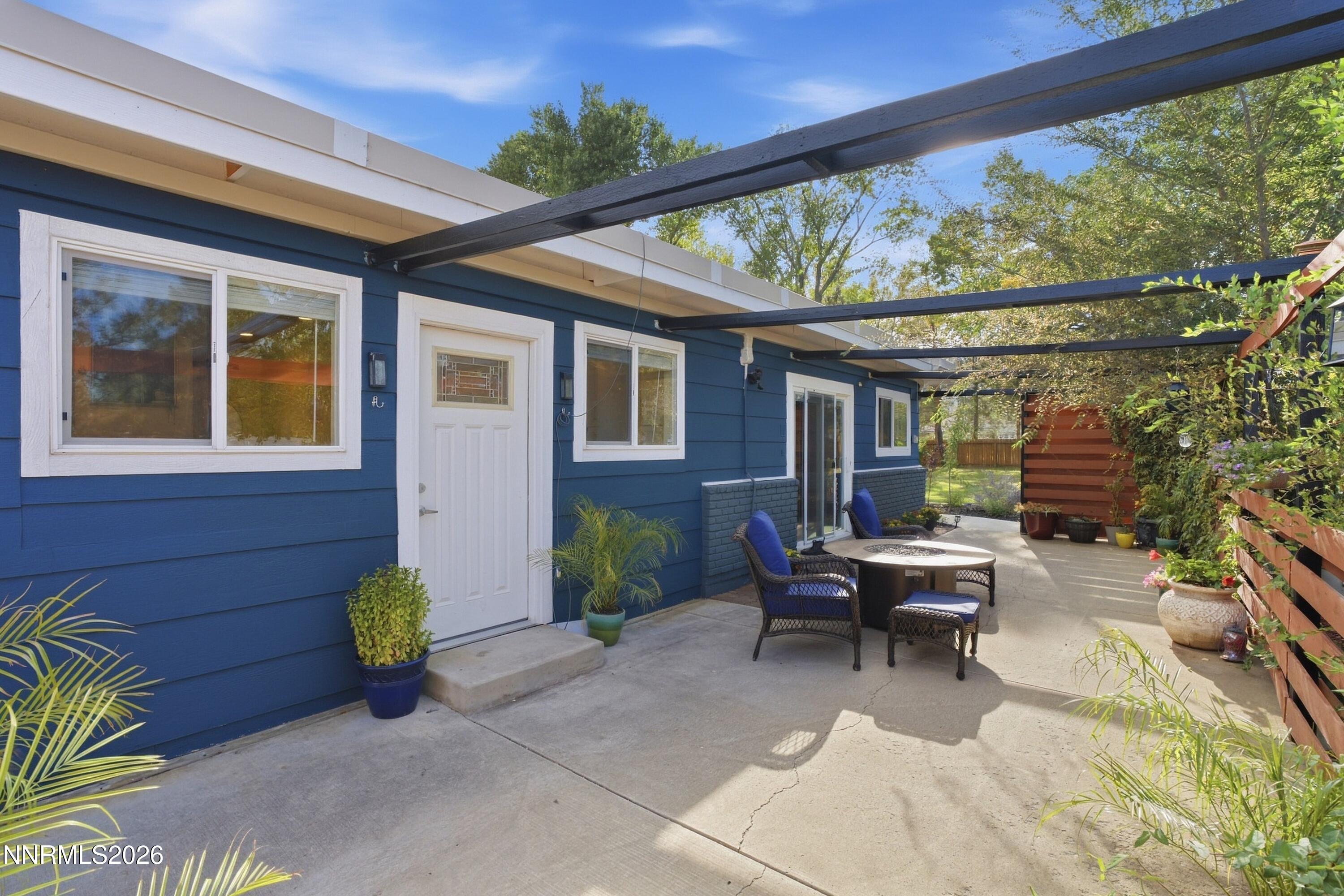 Blue-sided home with a pergola-covered concrete patio, outdoor seating, and potted plants.
