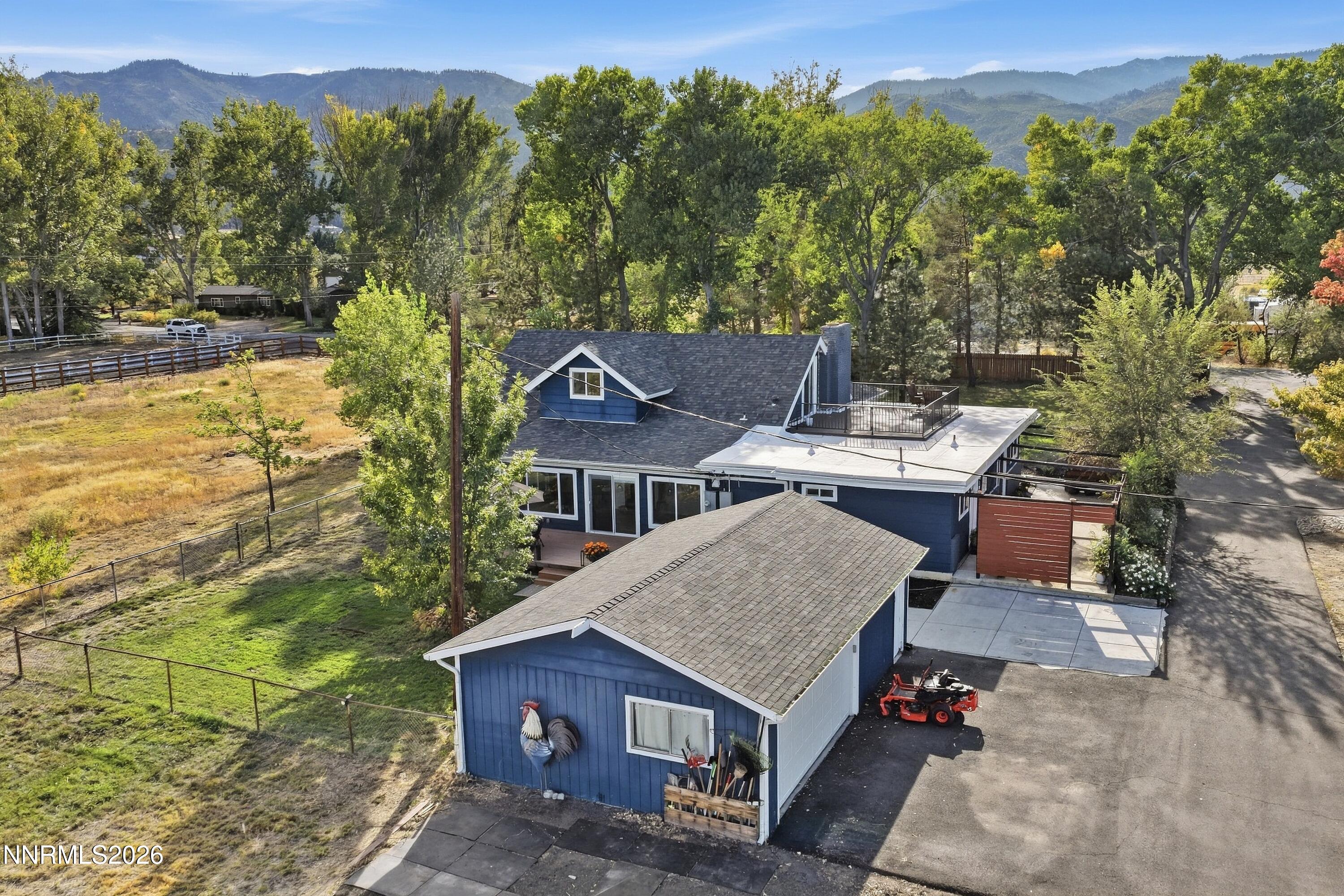 Blue house and outbuilding with rooftop deck, fenced yard, and mountains beyond.