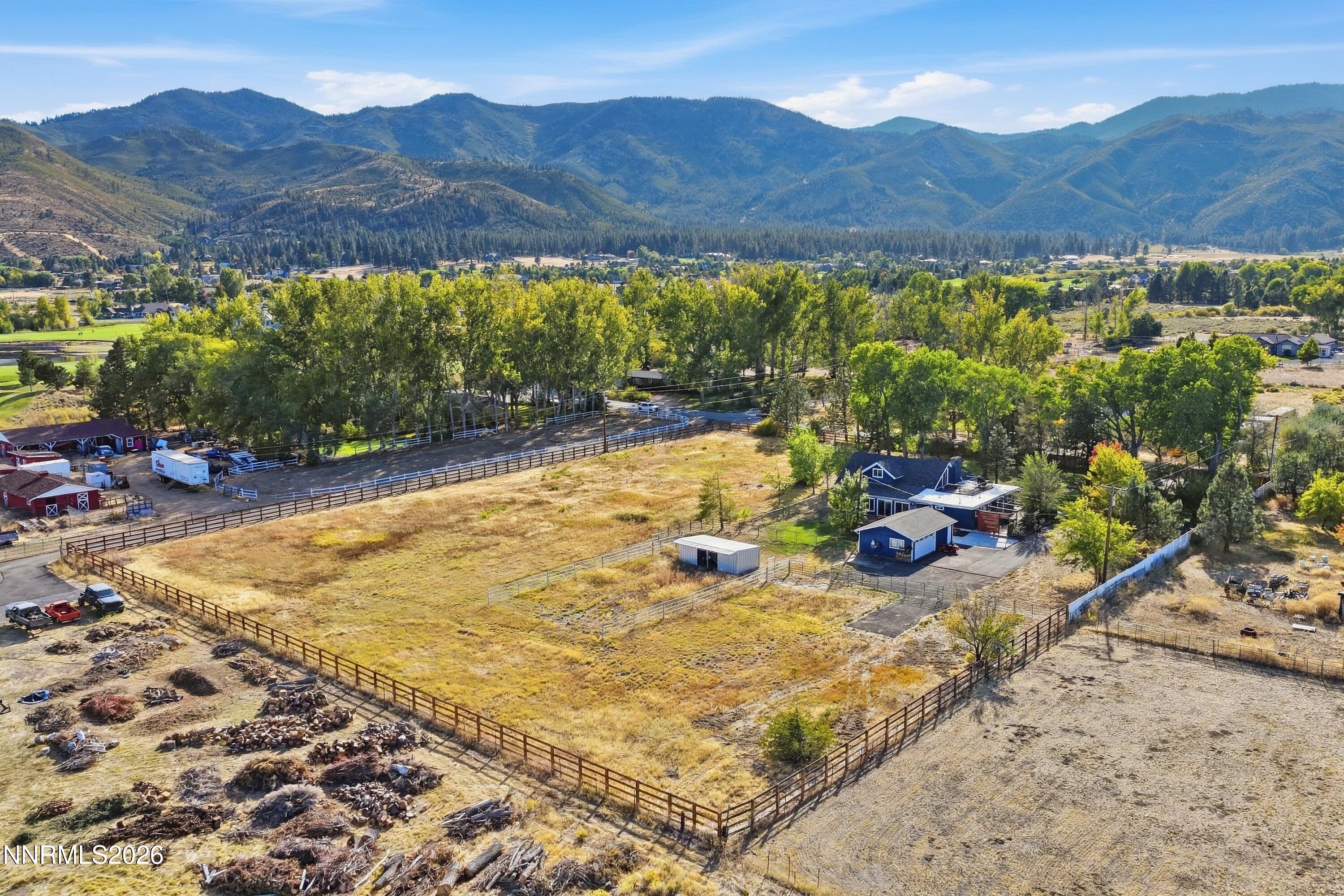 Aerial view of a fenced rural property with a house, outbuildings, and mountain views.